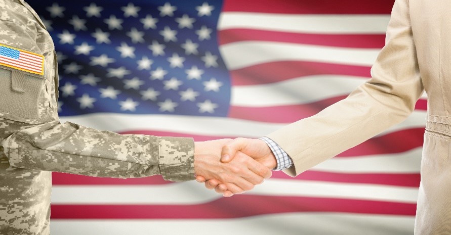 Two people shaking hands in front of an American flag.